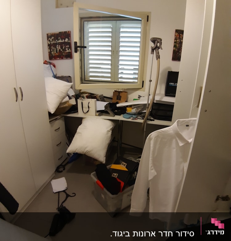 חדר מבולגן עם בגדים, כריות וארגזים על הרצפה